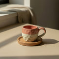 Eternal Pottery two-tone ceramic mug in coral and beige with textured finish and handle, shown on a wooden saucer.