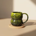 Eternal Pottery textured forest glow double bubble mug with handle on a wooden coaster.