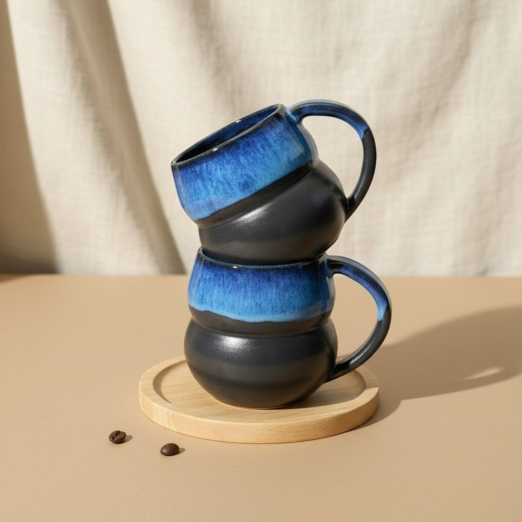 Two stacked textured midnight double bubble mugs with handles, resting on a wooden coaster. Eternal Pottery.