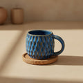 Eternal Pottery textured ocean blue fish scale mug with handle on a wooden coaster.