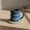 Eternal Pottery textured ocean triple bubble mug with handle on a wooden coaster.