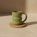 Eternal Pottery textured olive core triple bubble mug with handle on a wooden coaster.