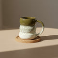 Eternal Pottery textured olive mist triple bubble mug with handle on a wooden coaster.