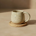 Eternal Pottery toasted sand round mug resting on wooden coaster.
