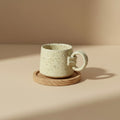 Eternal Pottery textured vanilla mist ring mug with handle on a wooden coaster.